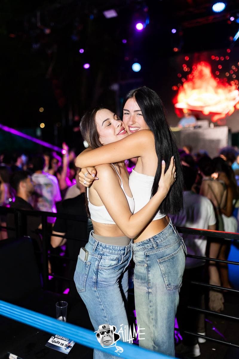 Due amiche si abbracciano ridendo, con le luci del palco alle spalle